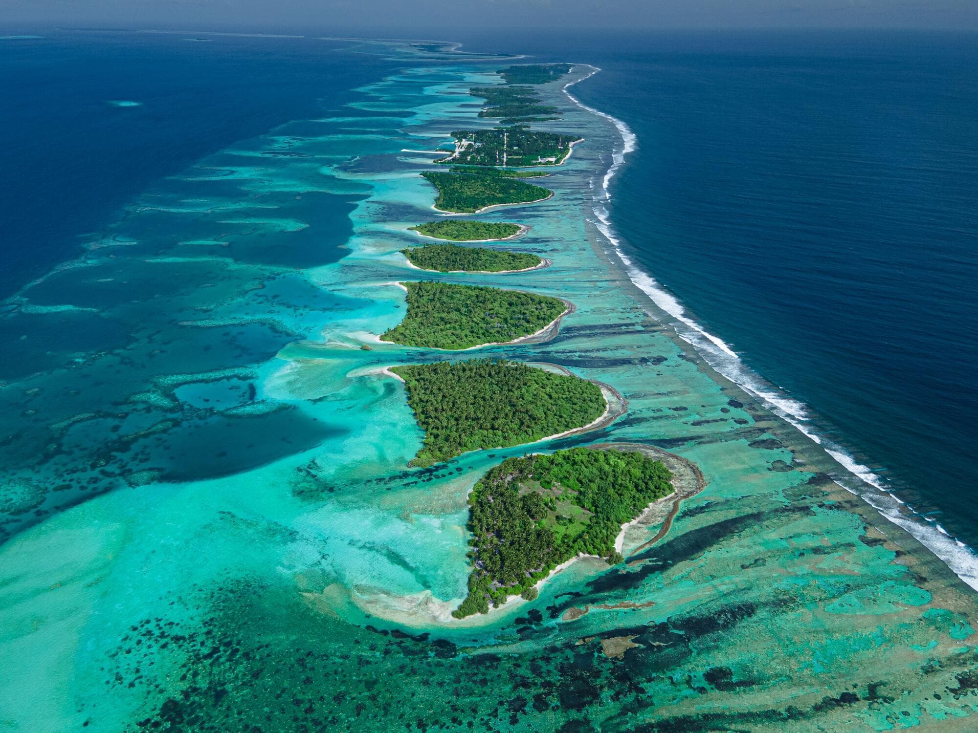 A chain of green islands along a reef, with a turquoise lagoon on one side and deep blue ocean on the other